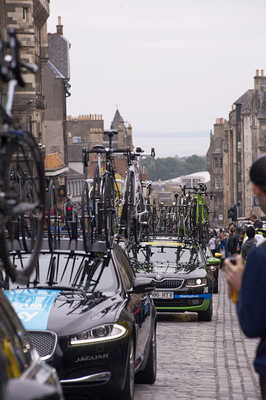 Team cars laden with bikes drive up the High Street 