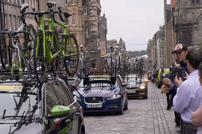 Team cars laden with bikes drive up the High Street