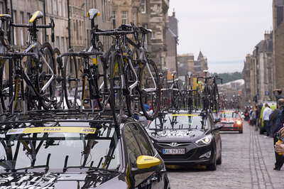 Team cars laden with bikes drive up the High Street