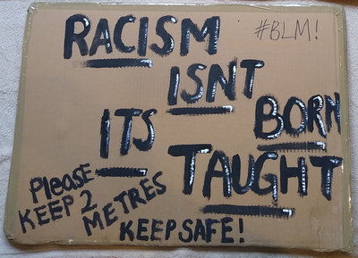 Cardboard placard reads 'Racism isn't born it's taught