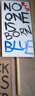 Placard on a pole reads 'No one is born blue'